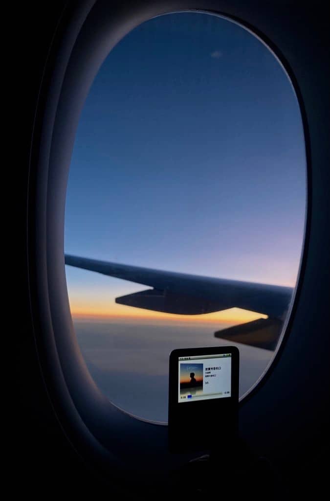 picture of airplane window of purple and orange sunset with an ipod player in front