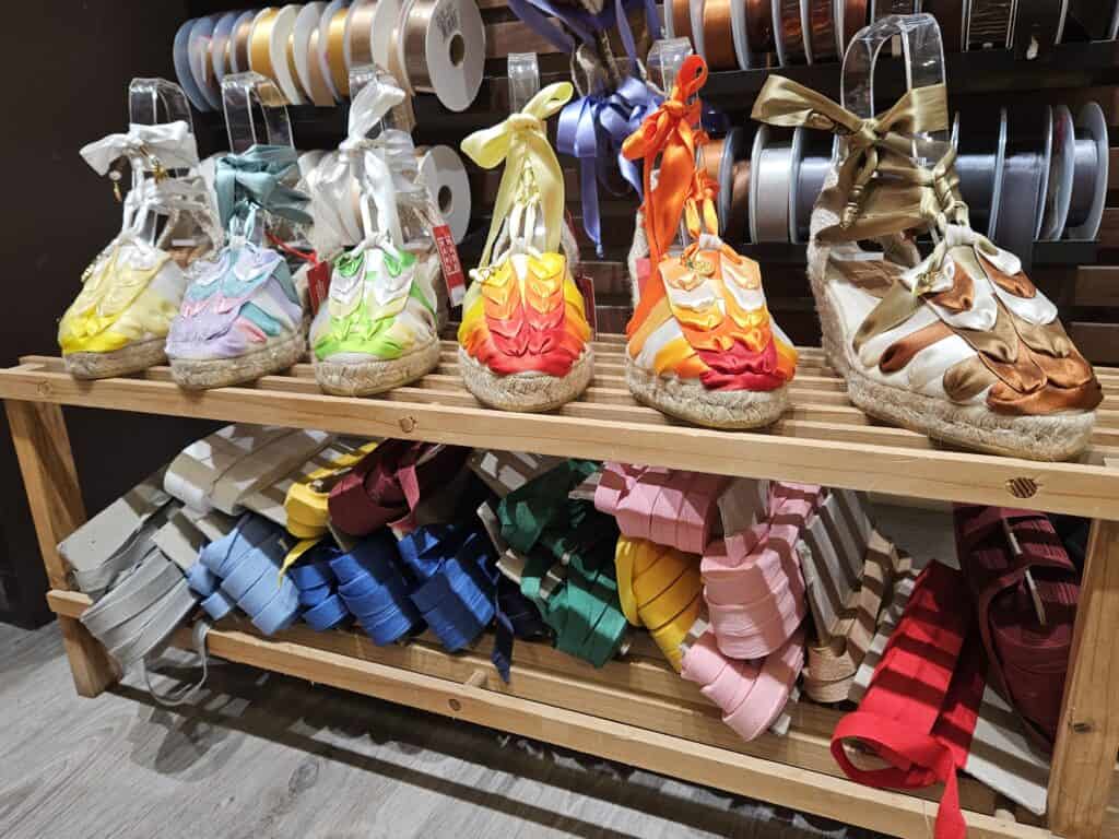 Espadrilles lined up on a shelf above a row of ribbons used to decorate them.