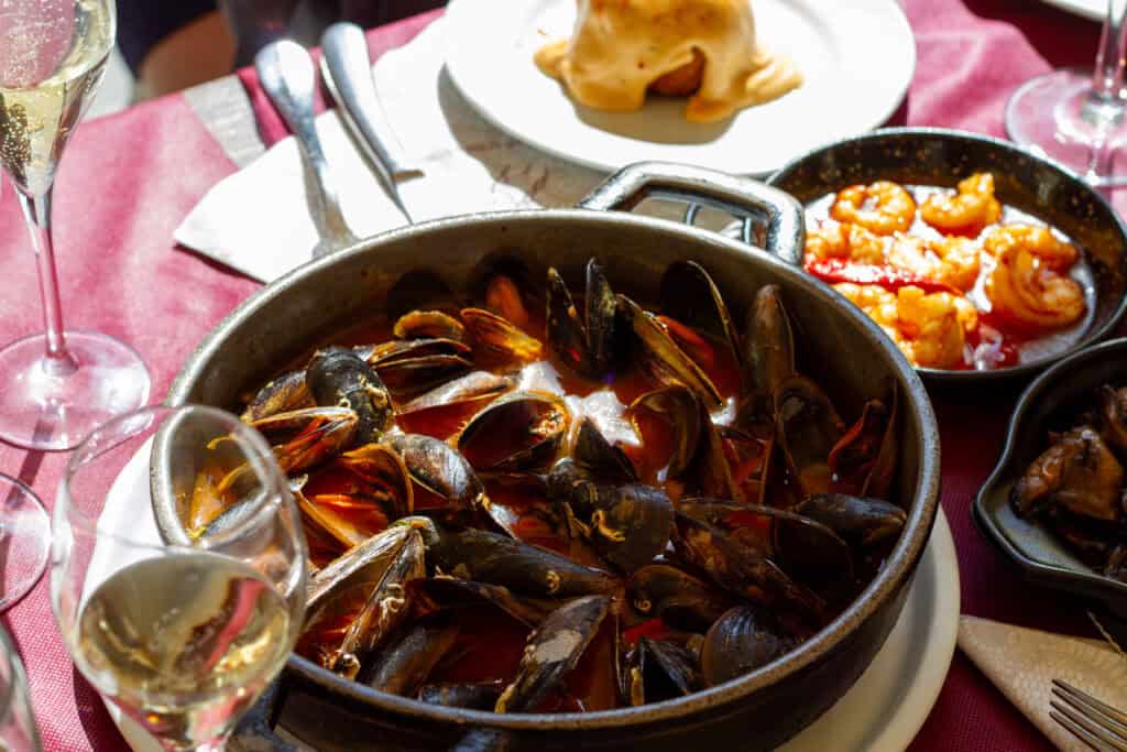 Close up photo of a large bowl of mussels, small bowl of shrimp, and other small dishes and drink on a table.