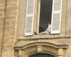 A man sitting on a windowsill watching people in the streets