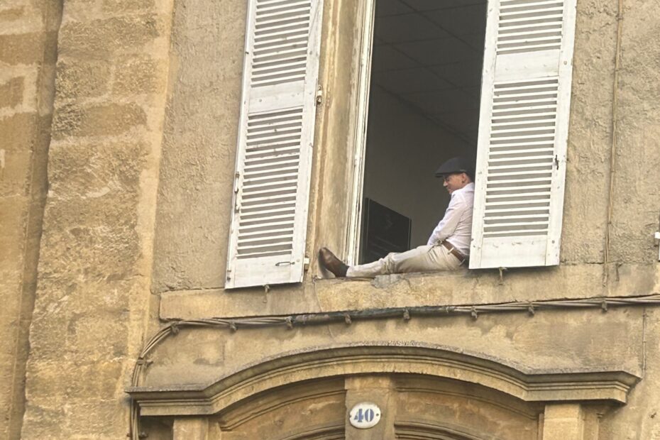 A man sitting on a windowsill watching people in the streets