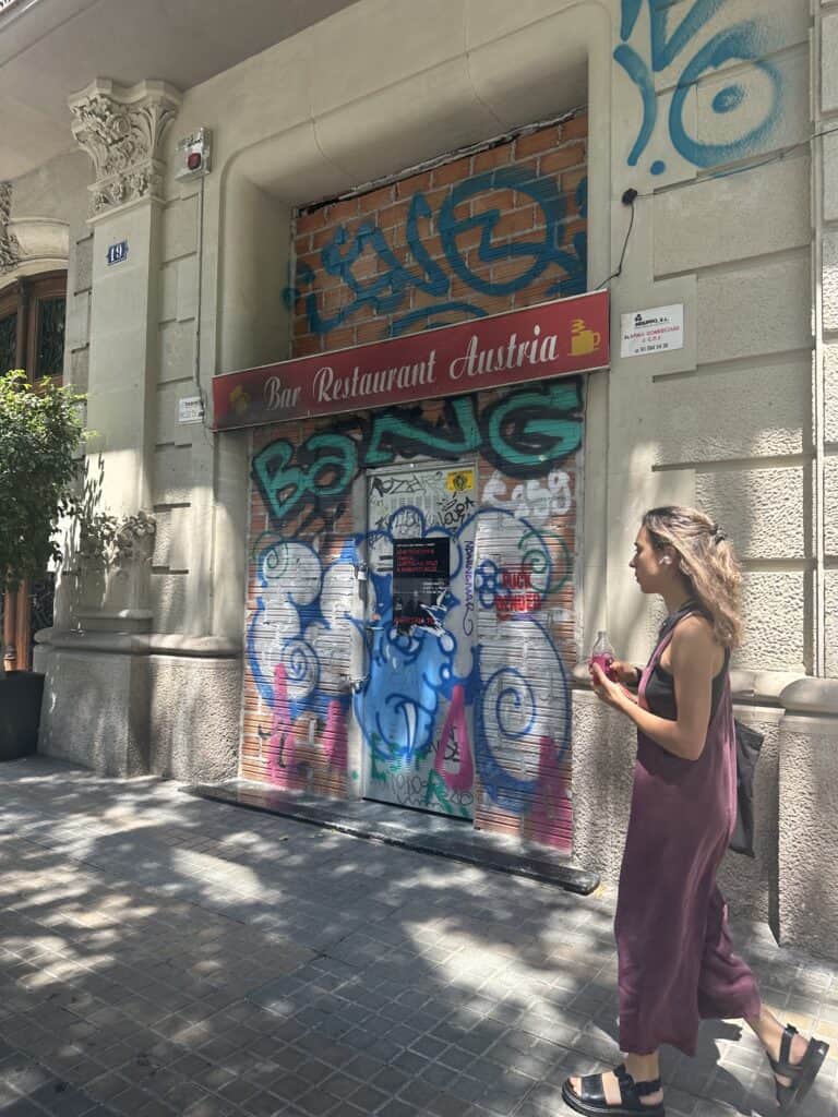 A woman walks past a door covered in graffiti artist tags.