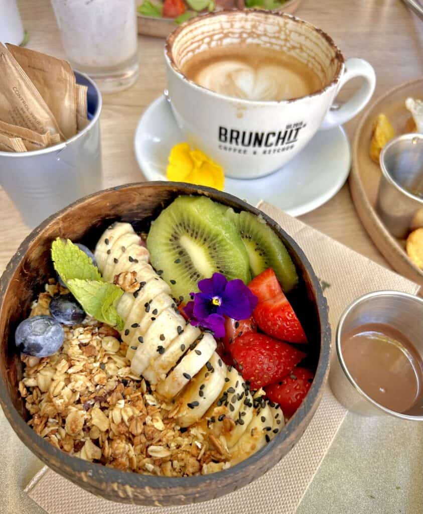 An açai bowl covered in fruits next to a coffee cup with a Brunch It logo. 