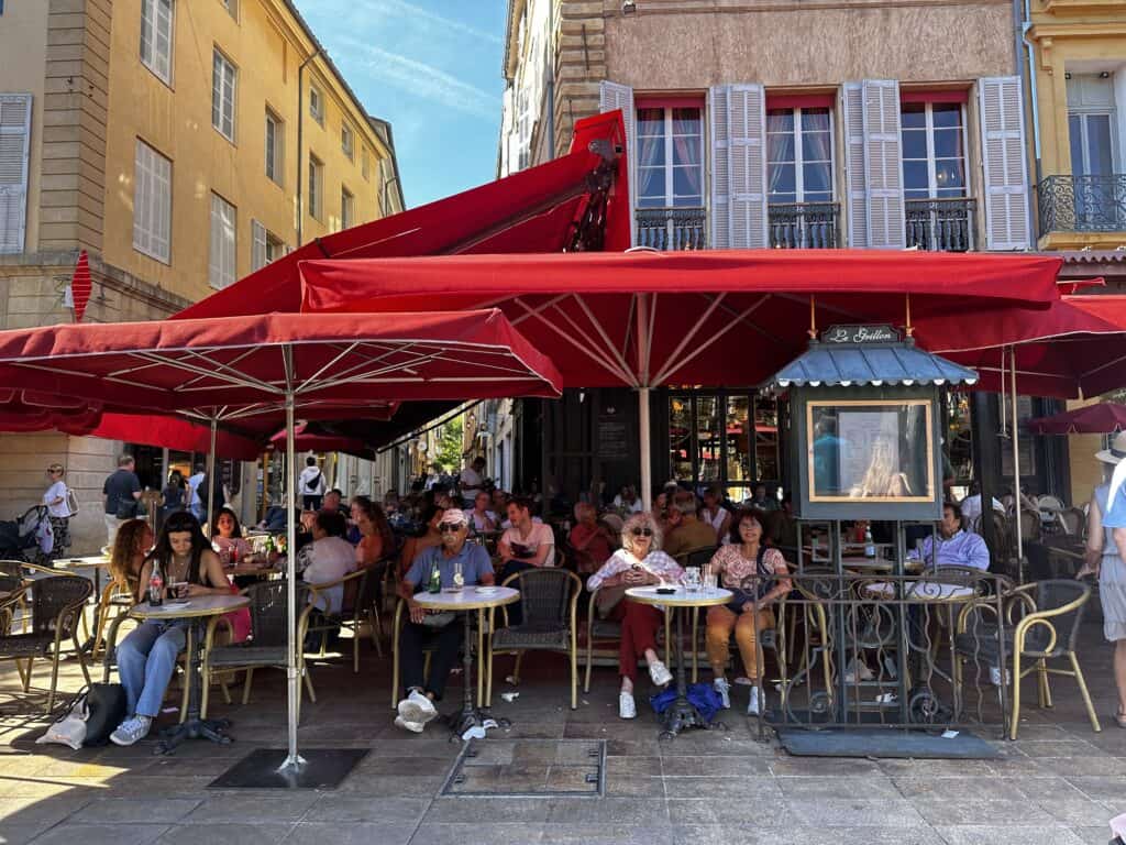 An outsidefrench cafe filled with customers with a red umbrella