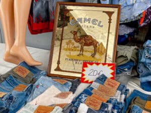 second-hand Levi jeans, mannequin legs, and a Camel Cigarette sign sit at a table at the market.