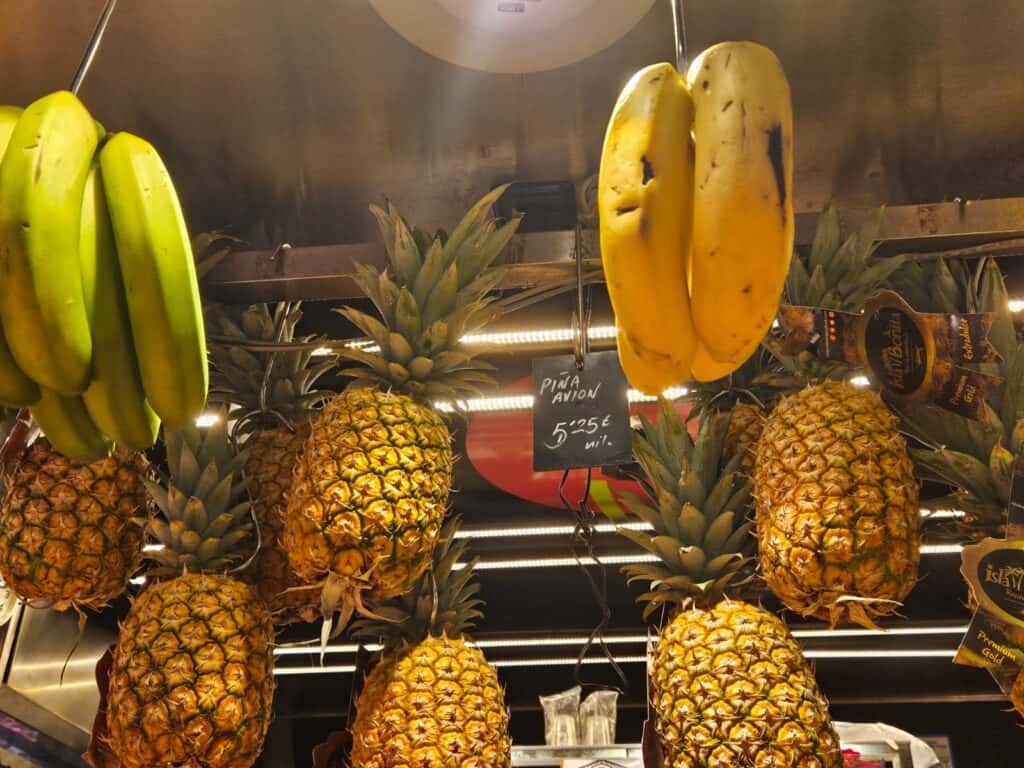 Pineapples and bananas hanging from market stall.