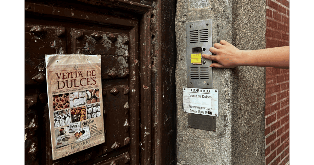 An image of the brown wooden door to the Reposteria. A hand leans in to ring the doorbell. On the door, a poster reading, "Venta De Dulces" depicts various types of desserts.