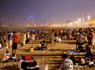 Crowds gather along the beach, watching the skies come alive with color and shimmer.